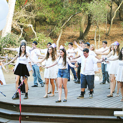 teens wearing white shirts performing on a stage outside.